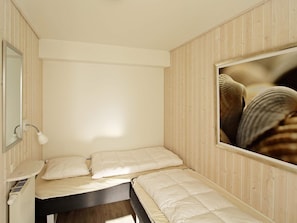 Habitació petita amb un llit individual, un panell de paret de fusta, un mirall, una làmpada de nit i una fotografia emmarcada.