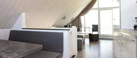A modern loft-style room with a dining area, kitchenette, and seating space.