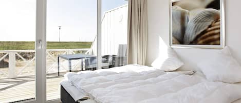 A bedroom with a large bed, a view of the beach, and a framed picture on the wall.