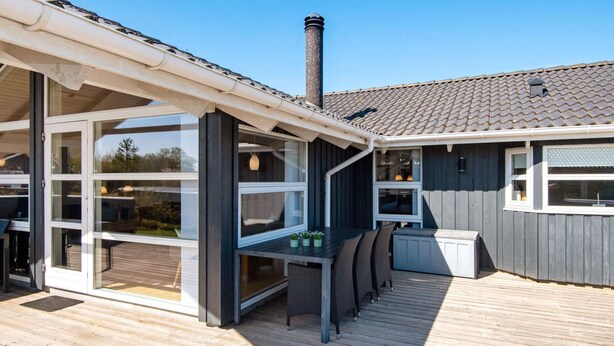 A modern outdoor deck with a glass enclosure, a built-in table and chairs, and a chimney. - 4 Star Holiday Home in Hemmet (Hemmet)