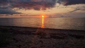A sunset over a calm sea with a beach in the foreground. - 4 Star Holiday Home in Hemmet (Hemmet)