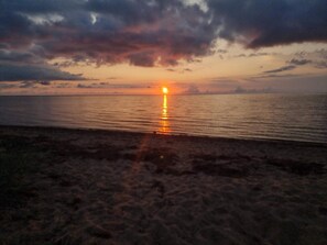 A sunset over a calm sea with a beach in the foreground.