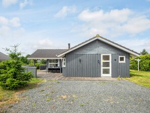 Et moderne hus med grå facade, en træterrasse og en grusindkørsel.
