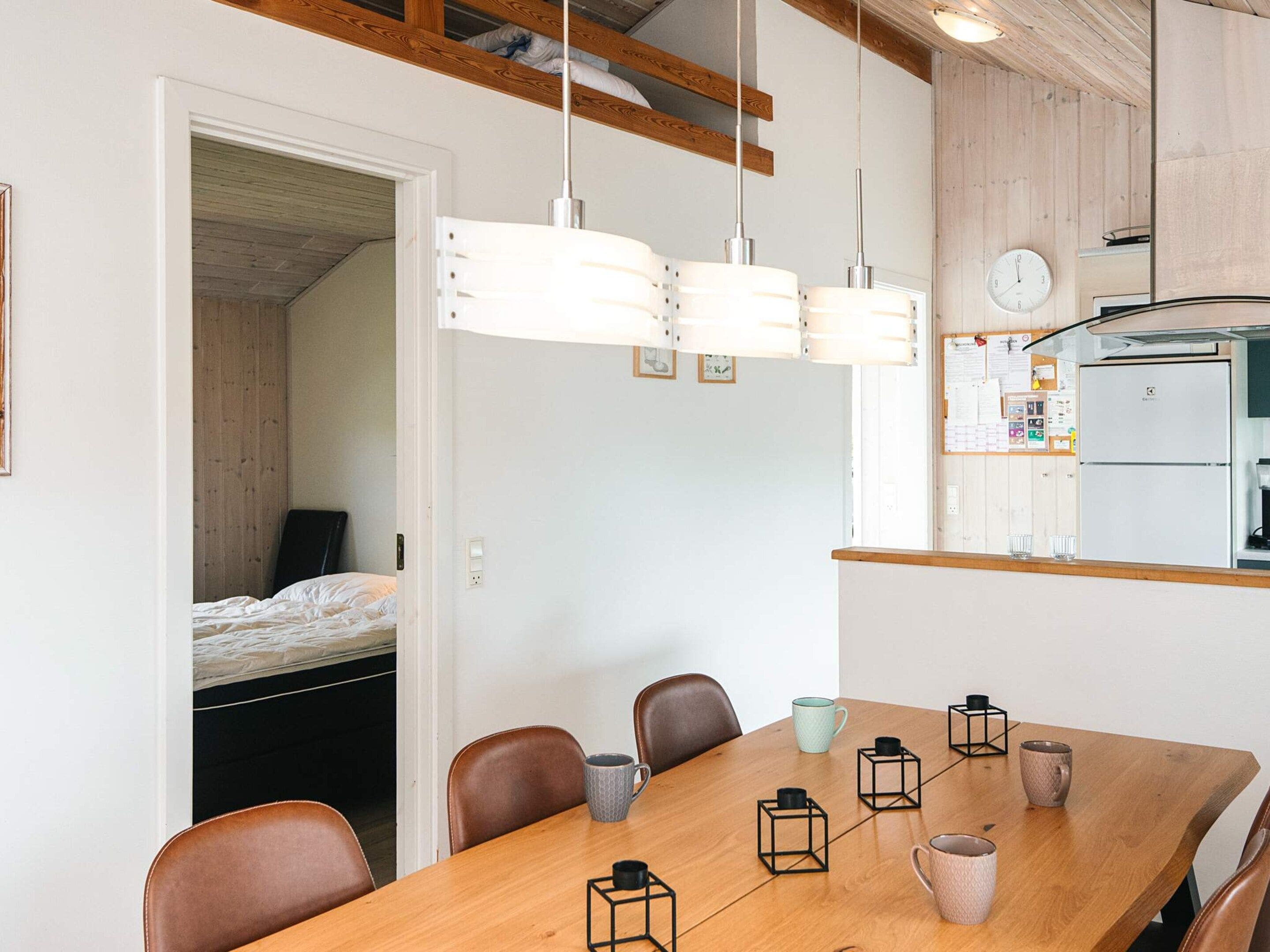 Un espace de vie compact comprenant une table à manger en bois, des chaises, un coin cuisine et un lit dans la pièce adjacente.