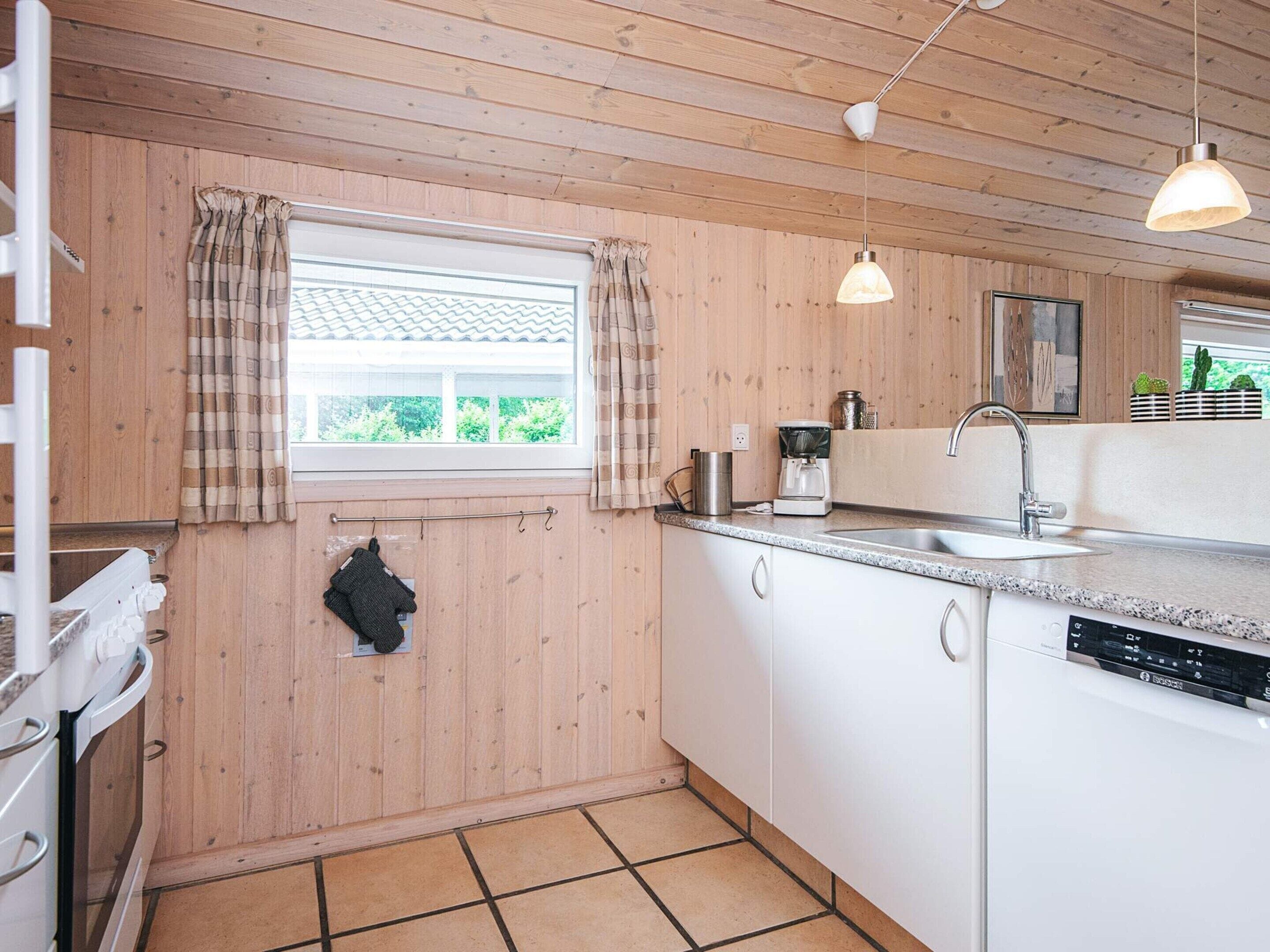 A kitchen with wooden walls, a window with curtains, a sink, a coffee maker, and a dishwasher.