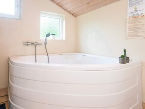 A bathroom with a large bathtub, a window, and a small potted plant on the wall.