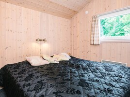 Un dormitorio con paredes de madera, una cama con colcha floral negra, dos lámparas de noche y una ventana con vistas a la vegetación.