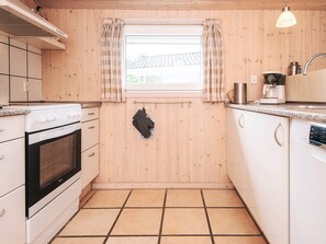 Eine kleine Küche mit Herd, Backofen und einem Fenster mit Vorhängen.