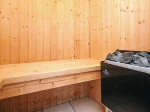 A sauna room with wooden walls, a bench, and a black heater.