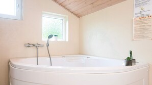 A bathroom with a large bathtub, a window, and a small potted plant on the wall. - 4 Star Holiday Home in Oksbol (Oksbol)