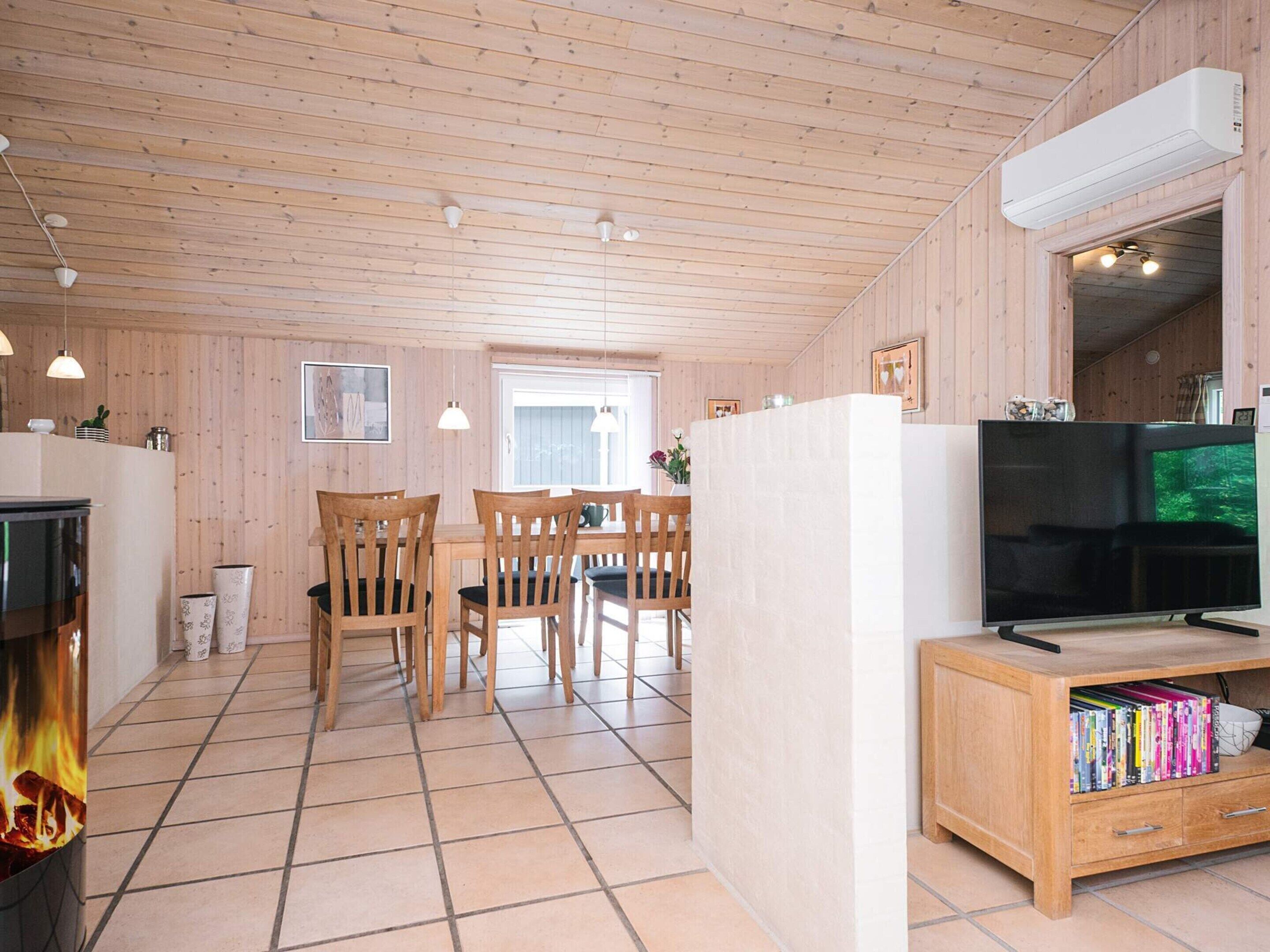 A wooden-paneled room with a dining table, chairs, a television, and a bookshelf.