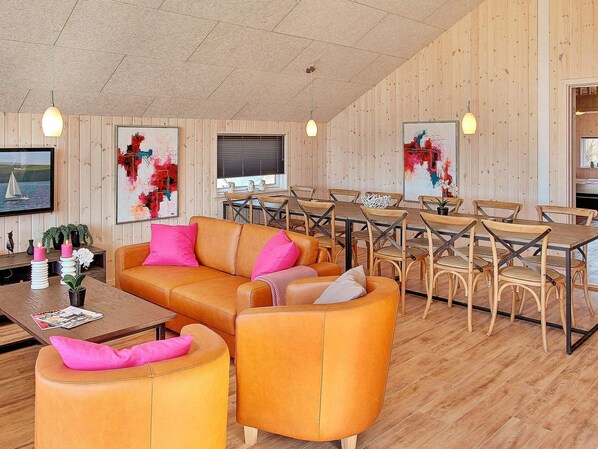 Un intérieur moderne avec un mur recouvert de panneaux en bois, un canapé d’angle, une table à manger avec des chaises et des œuvres d’art accrochées aux murs.