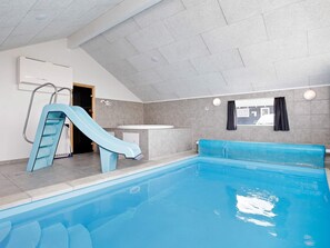 An indoor swimming pool with a slide, a changing room, and a window with curtains.