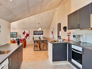 A modern kitchen with a central island, built-in appliances, and a dining area with wooden flooring and chairs.