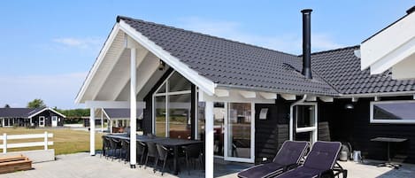 Una casa moderna con porche cubierto, mobiliario exterior y chimenea.