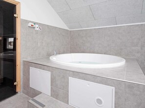 A modern bathroom with a freestanding bathtub, grey tiles, and a wooden door.