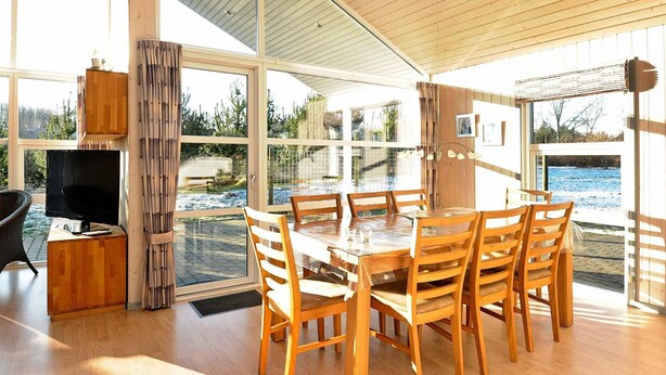 A spacious room with a large wooden table and chairs, a television on a wooden stand, and large windows offering a view of a snowy outdoor area.