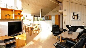 A spacious living area with a wooden ceiling, a dining table, and a black leather sofa.
