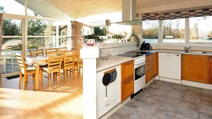 A modern kitchen with wooden cabinets, a built-in oven, and a large window overlooking a snowy landscape.