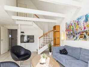 A living room with a staircase, a flat-screen TV, a modern chair, a sofa, and a colorful abstract painting. - 5 Star Holiday Home in Blokhus (Blokhus)