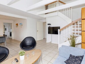 A spacious living area with a modern staircase, a flat-screen TV mounted on the wall, and a dining area with a table and chairs. - 5 Star Holiday Home in Blokhus (Blokhus)