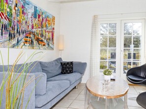 A living room with a blue sofa, a glass coffee table, and a colorful abstract painting on the wall. - 5 Star Holiday Home in Blokhus (Blokhus)