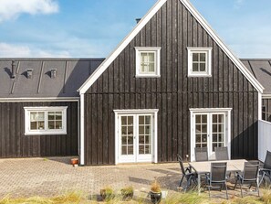 A dark wooden building with white trim, large windows, and a paved patio area with outdoor seating. - 5 Star Holiday Home in Blokhus (Blokhus)