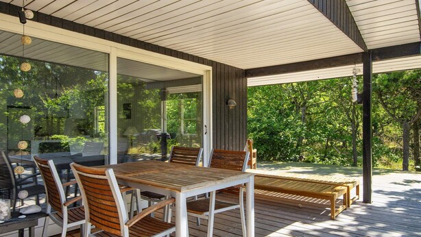 An outdoor patio with a wooden table and chairs, a glass enclosure, and a view of greenery. - 5 Person Holiday Home in Glesborg-by Traum (Glesborg)
