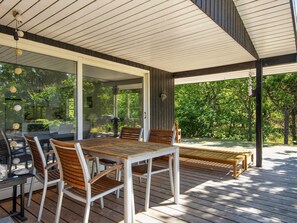 An outdoor patio with a wooden table and chairs, a glass enclosure, and a view of greenery. - 5 Person Holiday Home in Glesborg-by Traum (Glesborg)