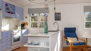 A compact kitchen with a built-in island, a dining area with a blue chair, and a view of the outdoors through large windows. - 5 Person Holiday Home in Glesborg-by Traum (Glesborg)