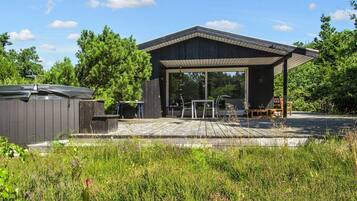 A covered outdoor patio with a table and chairs, surrounded by a wooden deck and lush greenery.