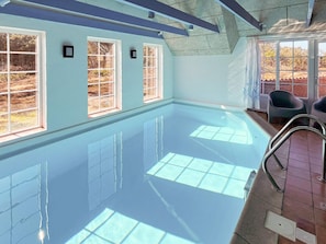 A swimming pool with clear water, surrounded by windows with a view of trees.