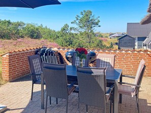 An outdoor patio with a brick wall, a grill, and a table set with chairs. - 4 Star Holiday Home in Ringkobing (Ringkobing)