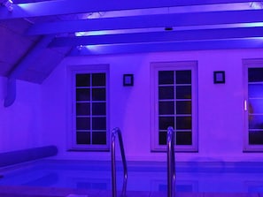A swimming pool area with a blue hue, two windows, and a metal ladder. - 4 Star Holiday Home in Ringkobing (Ringkobing)