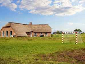 A thatched-roof house with a brick exterior, a small attached structure, and a field in the foreground. - 12 Person Holiday Home in Ringkobing-by Traum (Ringkobing)