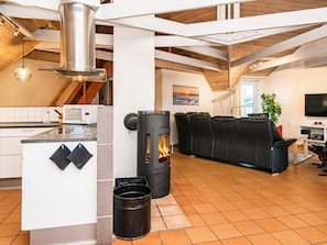 Uma cozinha moderna com fogão central, sala de jantar com sofá preto e televisão na sala de estar.