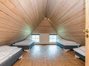 Una habitación con dos camas, piso de madera y techo inclinado.