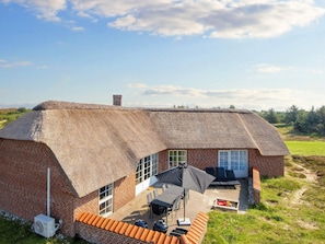 A thatched-roof house with a brick exterior, a patio with outdoor furniture, and a clear view of the surrounding landscape. - 4 Star Holiday Home in Ringkobing (Ringkobing)