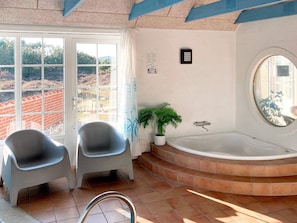 A bathroom with a bathtub, two chairs, a potted plant, and a view of a brick wall outside. - 12 Person Holiday Home in Ringkobing-by Traum (Ringkobing)