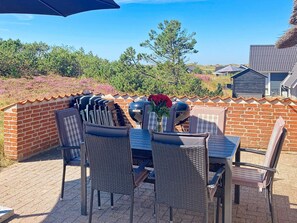 An outdoor patio with a brick wall, a table with chairs, and a grill. - 4 Star Holiday Home in Ringkobing (Ringkobing)