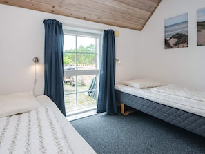 Quarto com cama, janela com cortinas, vista do exterior e uma pequena mesa com cadeira do lado de fora.