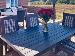 A patio with a table and chairs, a vase with red roses, and a brick wall in the background.