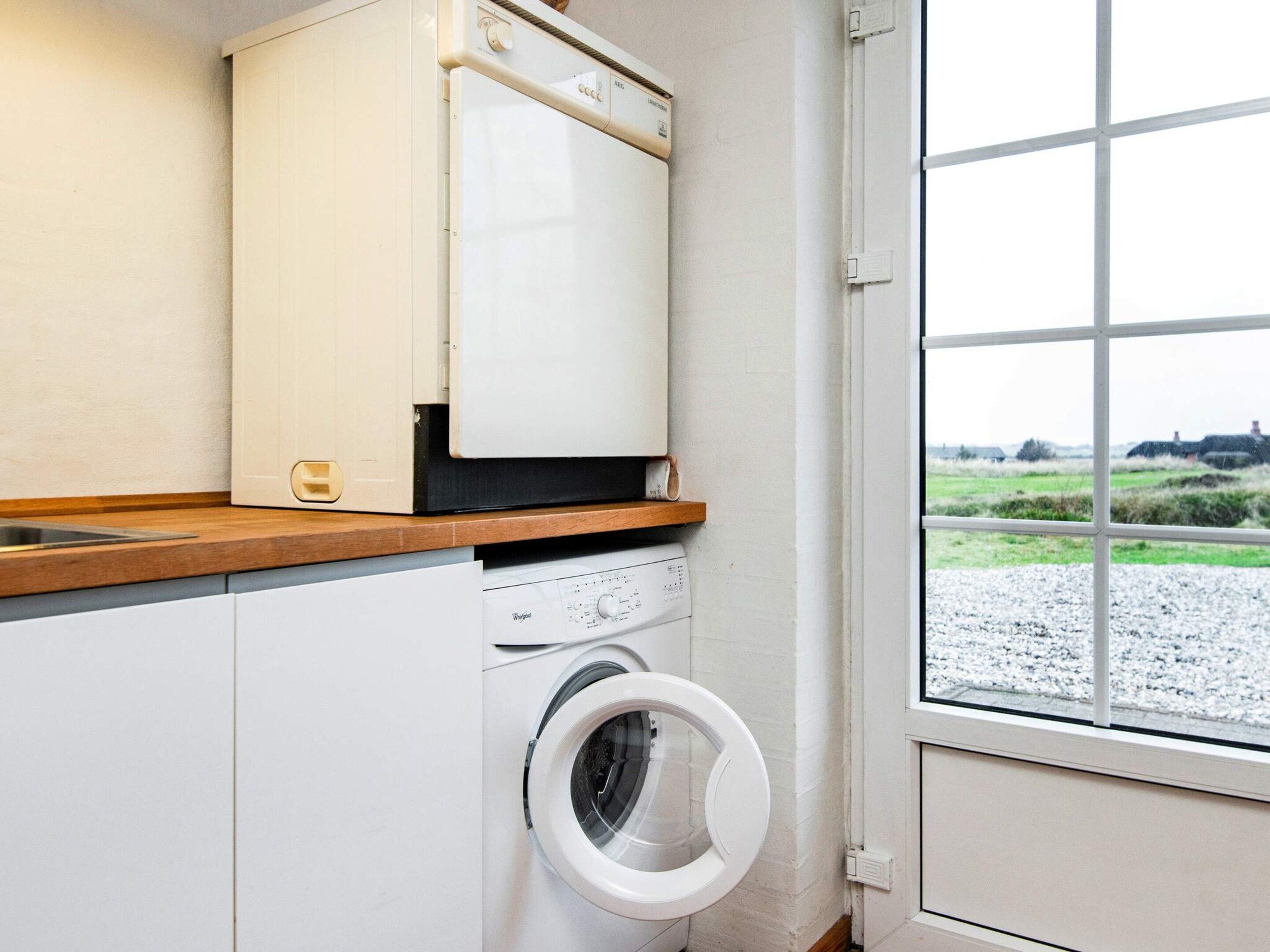 A laundry room with a washing machine, a dryer, and a window with a view of a rural landscape.
