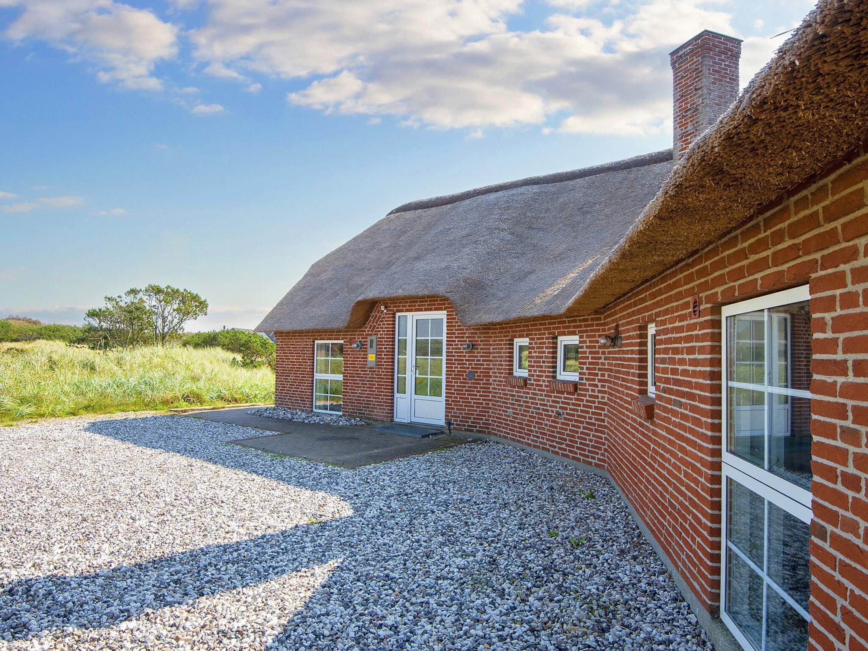 A brick building with a thatched roof, a gravel driveway, and a clear sky.