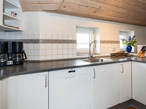 A modern kitchen with white cabinets, a black countertop, a coffee maker, and a sink. - 4 Star Holiday Home in Ringkobing (Ringkobing)