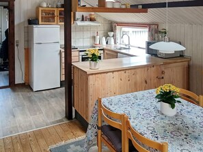 Kompakti keittiö, jossa on puukalusteet, valkoinen jääkaappi, pesuallas sekä ruokailutila, jossa on pöytä ja tuolit.