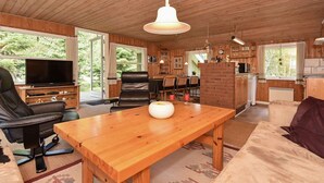 A spacious living area with a wooden dining table, leather chairs, a sofa, and a television.