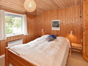 Une chambre à coucher aux murs lambrissés, avec un lit, une fenêtre, un tableau accroché au mur et une table de chevet avec une lampe.