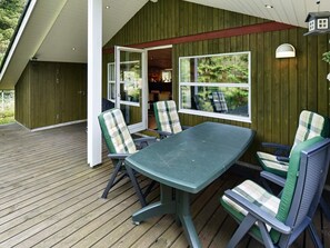 Un espace extérieur abrité, aménagé avec une table et des chaises, un sol en bois et offrant une vue sur la végétation environnante.