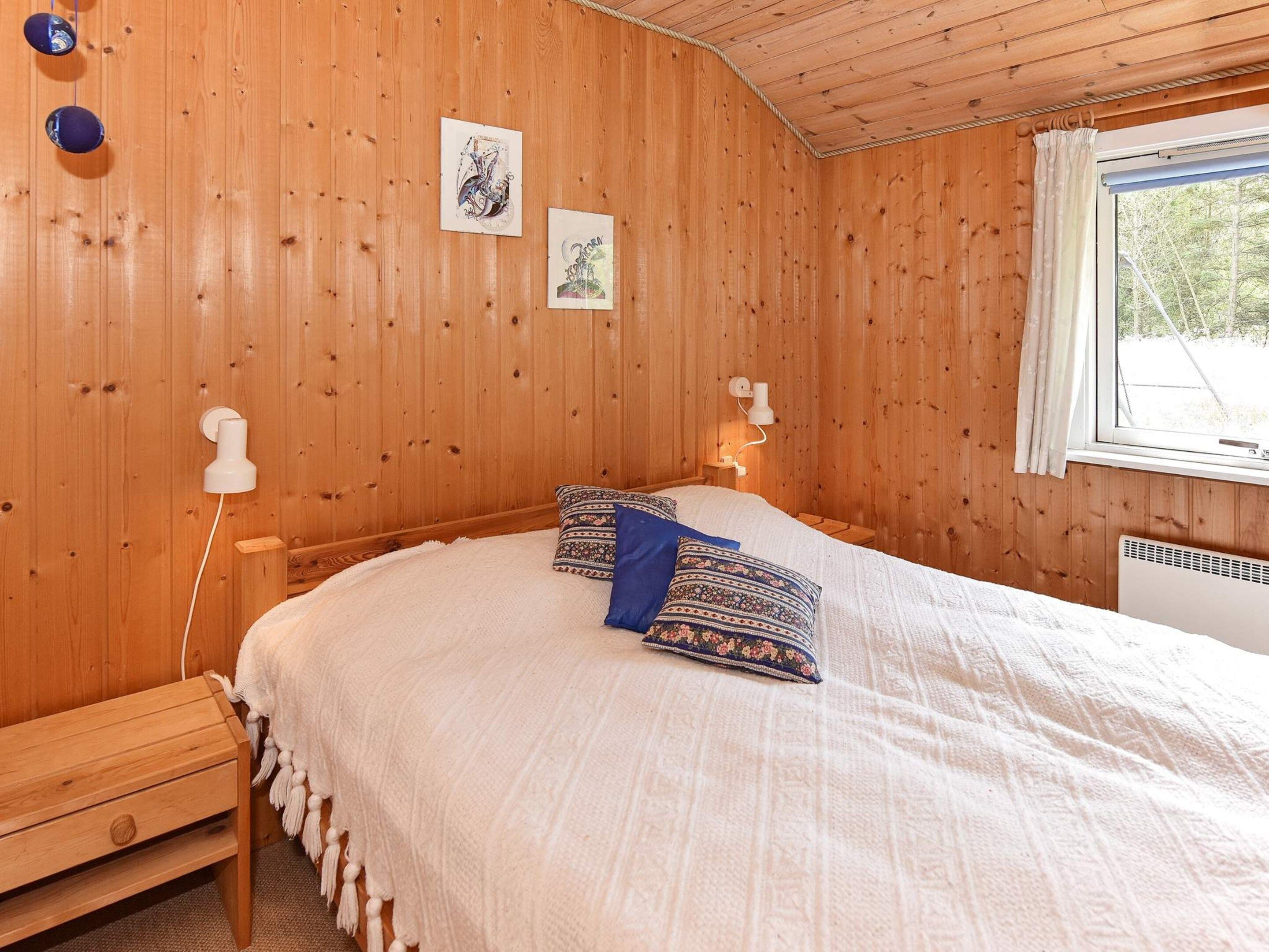 A wooden-paneled bedroom with a bed, two wall-mounted lamps, and a window with curtains.
